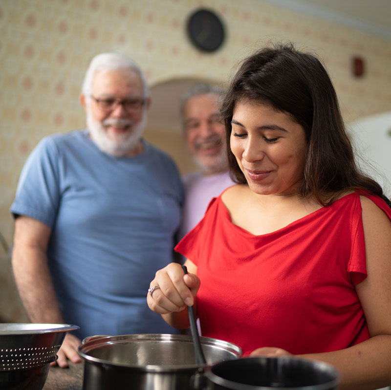 Woman cooking in kitchen while chatting with with senior couple 
